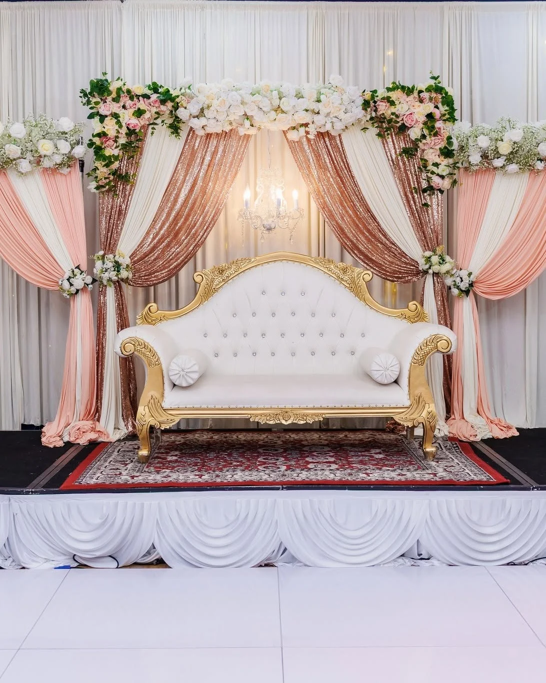 A decorated celebration stage with peach draping and white flowers