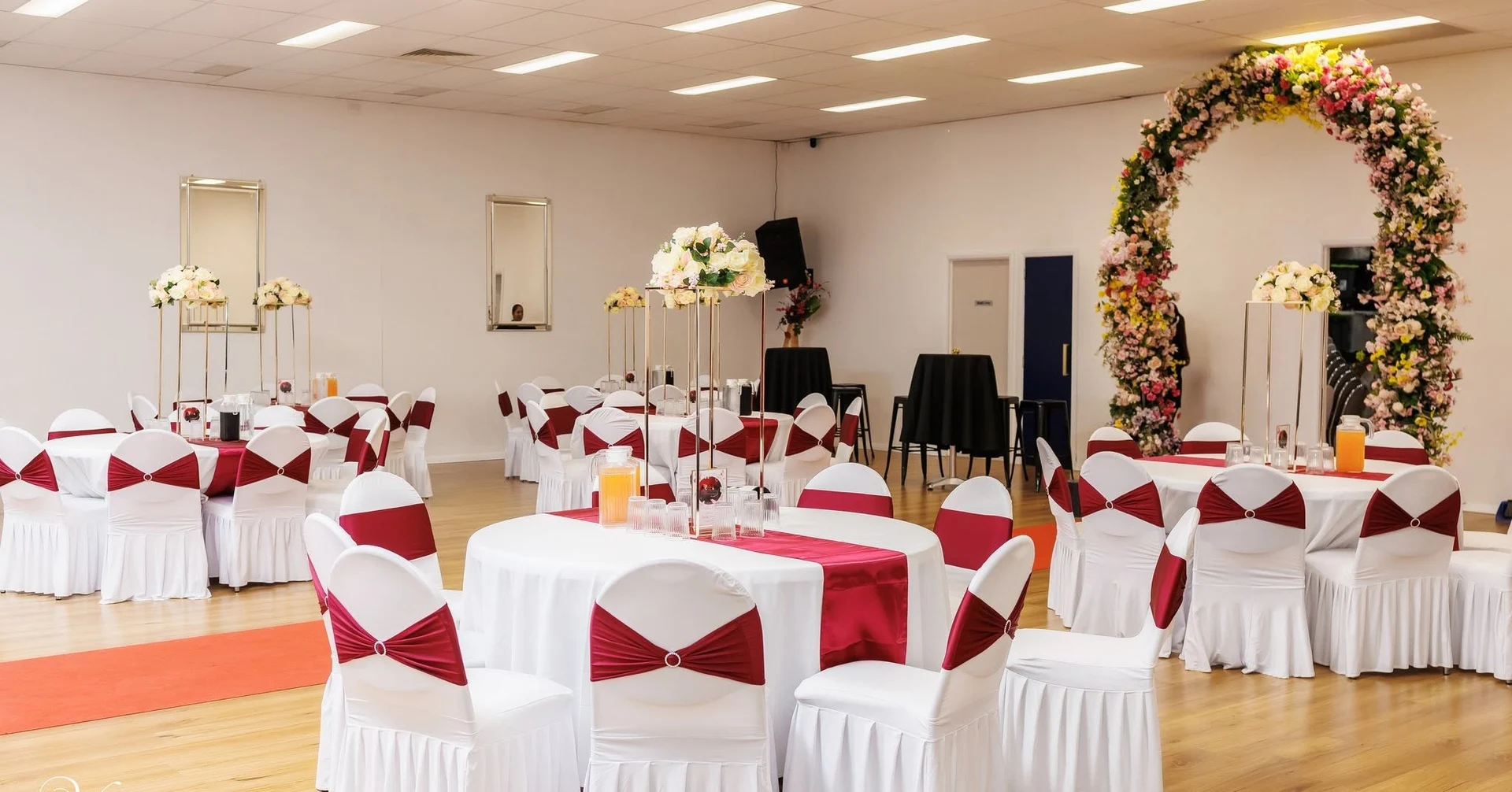 KTM Banquets reception tables with burgundy chair sashes and a floral arch
