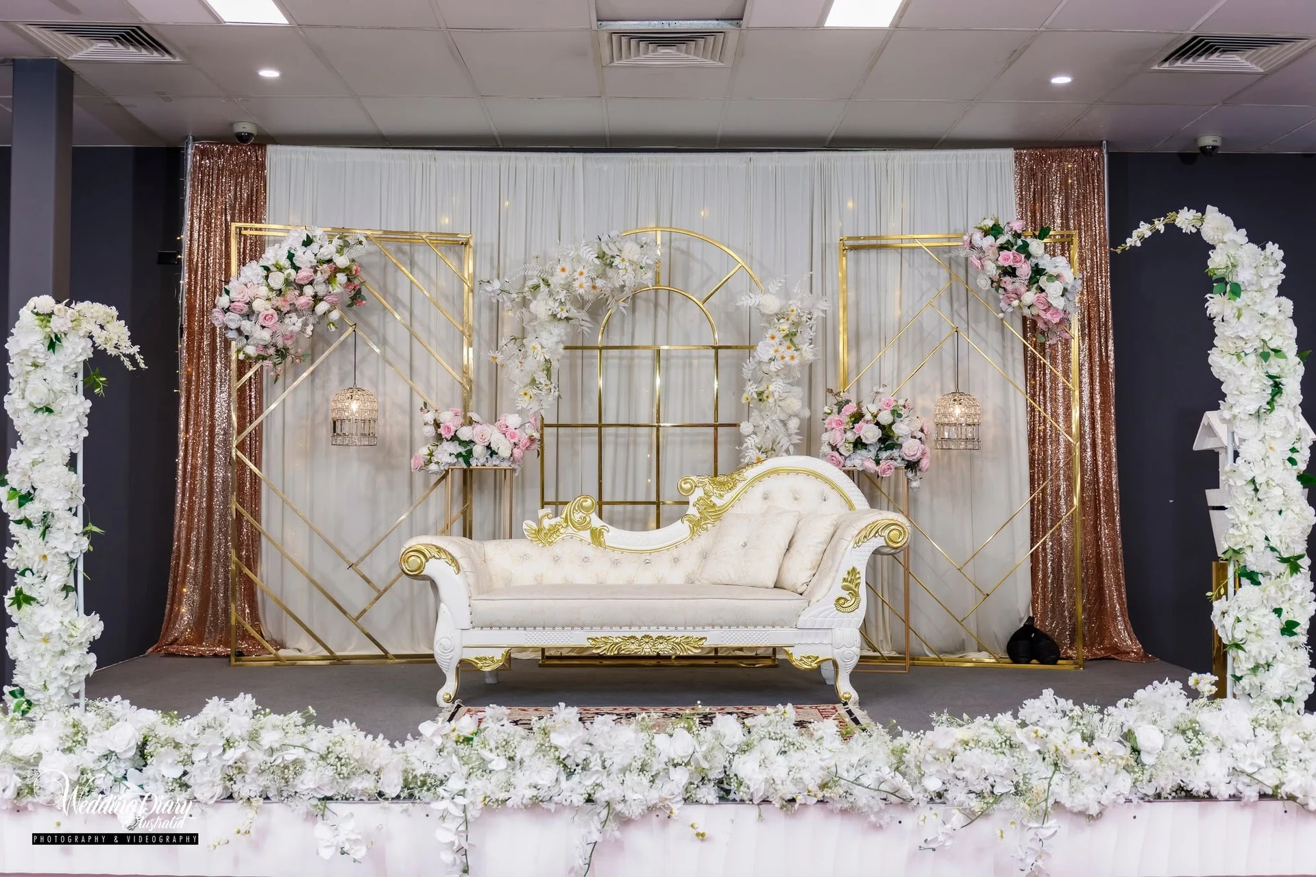 White and gold chaise on a decorated stage with floral columns and gold frames